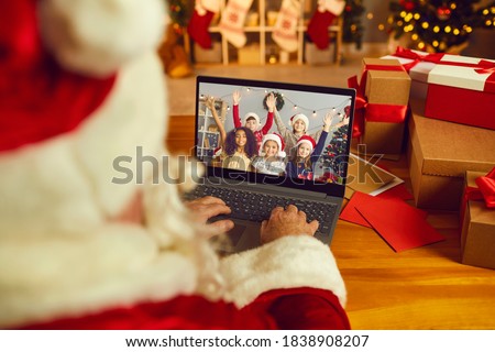 Over shoulder view of Santa Claus or Father Christmas having video call with happy diverse children on laptop computer in his workshop. Self-isolation and virtual online celebration at home concept