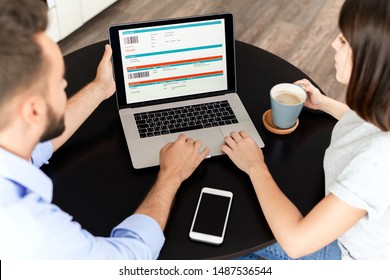 Over Shoulder View Of Serious Busy Young Couple Sitting At Round Table And Using Laptop While Checking Order Online