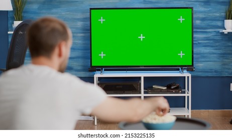 Over Shoulder View Of Sports Fan Watching Game On Green Screen Tv Mockup Encouraging Favourite Team Sitting On Couch. Man Sport Supporter Looking At Television With Chroma Key Display In Living Room.
