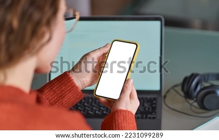 Over shoulder view of woman holding mobile phone with white blank mock up cellular screen applications working using cell phone. Cellphone display mock up for advertising apps concept.