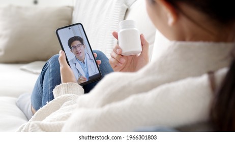 Over shoulder view of young asia woman talk to doctor on cellphone videocall conference medical app in telehealth telemedicine online service hospital quarantine social distance at home concept. - Powered by Shutterstock