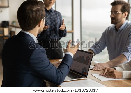 Over shoulder view of young businessman take part in corporate meeting, propose decision based on data at laptop screen. Diverse business team discuss statistical report infographics, charts share 商業照片 © 