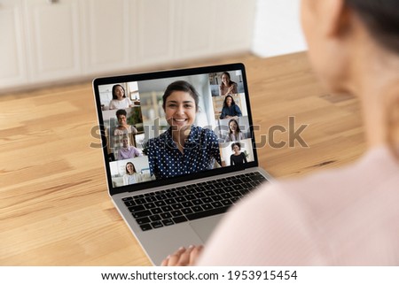 Over shoulder view of young lady sit by laptop pc screen take part in video conference psychological training for women. Diverse multiethnic group of young females meet online at virtual event webinar