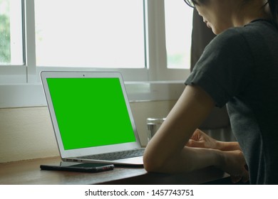 Over The Shoulder View Of Young Woman Sitting At Her Desk And Working On A Laptop With Green Screen.