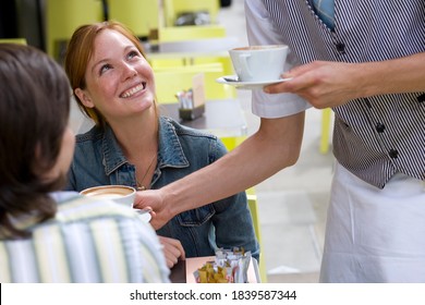 Over the shoulder waist up portrait of a young woman smiling at the waiter serving coffee at an outdoor caf�.