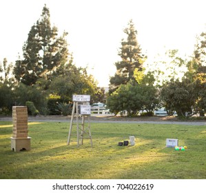 Over Sized Wood Block Stacking Game And Bocce Ball Set With A Light Box Sign On A Ladder Saying Playing For Keeps And Connect Four At A Lawn Party