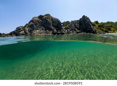 Over under split level view of crystal clear emerald turquoise sea water, rocky coast, and blue sky at Silistar beach, Strandzha Nature Park, Bulgaria.