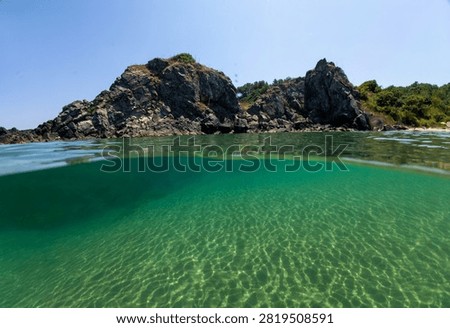 Over under split level view of crystal clear emerald turquoise sea water, rocky coast, and blue sky at Silistar beach, Strandzha Nature Park, Bulgaria.