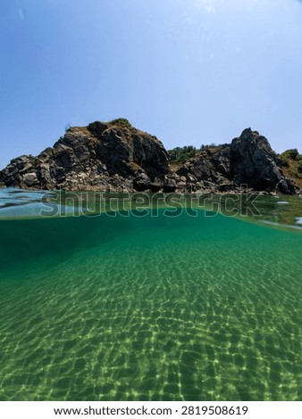 Over under split level view of crystal clear emerald turquoise sea water, rocky coast, and blue sky at Silistar beach, Strandzha Nature Park, Bulgaria.