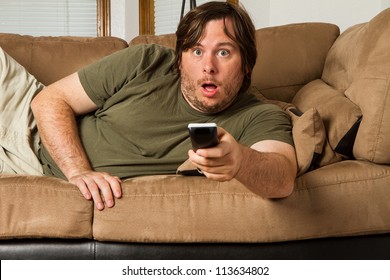 Over Weight Man Watching Something Shocking On TV. Could It Be Tabloids, Celebrity Gossip, A Movie, Or Something Else?