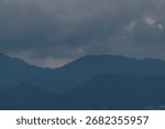 Overcast mountain range under a dramatic cloudy sky, showcasing a serene and vast natural landscape with subtle light.
