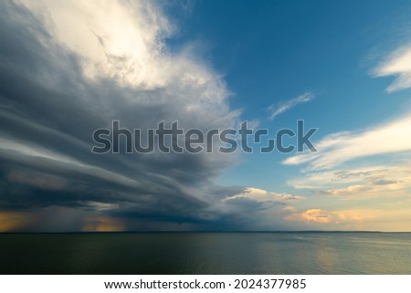 Overcast sky and heavy storm clouds over a wide river at sunset. Rain passing in the distance.