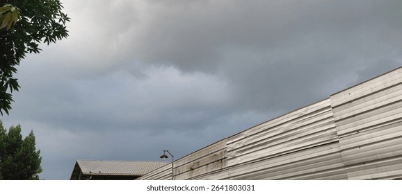 Overcast sky with subtle clouds above an aged industrial wall and distant building, framed by green foliage. Perfect for urban, weather, or subtle atmospheric themes. #CloudySky #UrbanTexture