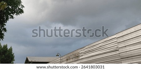 Overcast sky with subtle clouds above an aged industrial wall and distant building, framed by green foliage. Perfect for urban, weather, or subtle atmospheric themes. #CloudySky #UrbanTexture