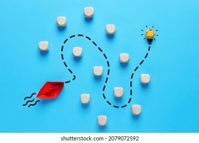 To overcome obstacles and to find a creative idea in business or education concept. Red paper boat finds a way to reach the light bulb by passing through the obstacles. - Shutterstock ID 2079072592