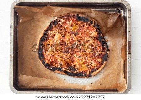 Overcooked and burnt pizza on a tray. Top view of a home made failed pizza.