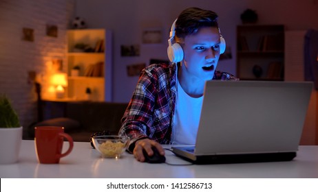 Overemotional Teen Playing Computer Game On Laptop And Eating Snacks, Addiction