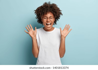 Overemotive Afro woman laughs loudly, hears funny joke or story, raises palms with satisfaction, dressed in casual white t shirt, being overjoyed, amused by friend. People and emotions concept - Shutterstock ID 1401813374