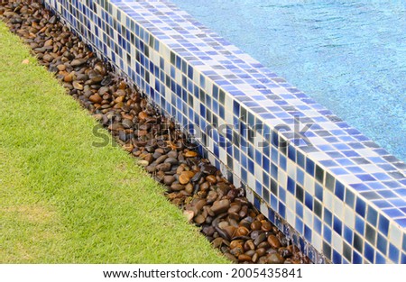 Overflow of Modern Blue Swimming Pool to Brown Gravel Gutter and Lawn