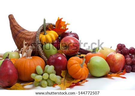 An overflowing cornucopia including pumpkins, grapes, gourds and leaves on a white background