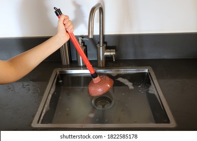 Overflowing kitchen sink, clogged drain. Hand holding plunger (force cup). Plumbing problems.