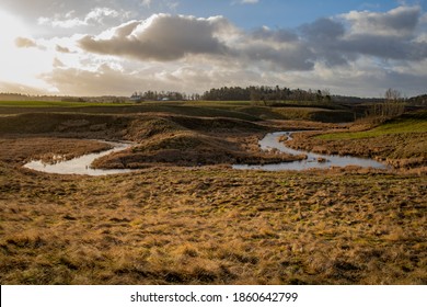 Overflowing river forms a bend in a rural landscape. Patches of sunlight shines on the scene with nice clouds at the horizon