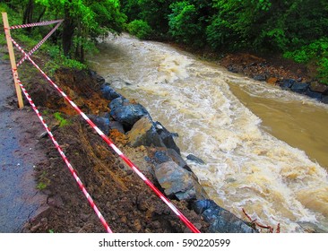 An Overflowing Stream Is Bounded By A Barricade Tape That Warns Of Impending Danger.