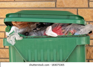 Overflowing Trash Can Against A Brick Wall