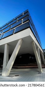 Overhanging Corner Of A Modern Office Building With Protruding Large Windows In An Ultra Wide Shot With A Bright Blue Sky In The Background.