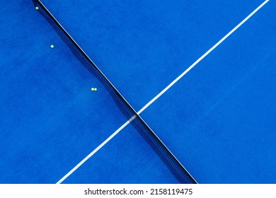 Overhead aerial photo of a blue paddle tennis court with three balls near the net.