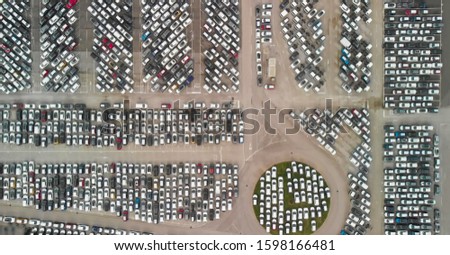 Overhead aerial view photo vehicle lot showing new produced cars by automakers stored there for further distribution towards car dealers port area where ships bring vehicles in mass production scene.