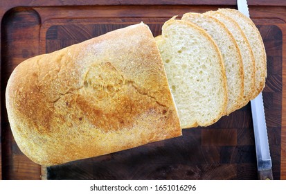 Overhead angle, Loaf of fresh home made bread, sliced bread, on dark cutting board,  with serrated edge knife towards the side.