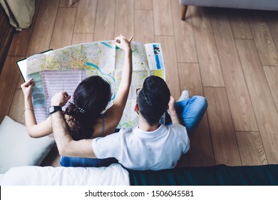 Overhead Back View Of Romantic Couple Relaxing On Wooden Floor Looking Down At Paper Map And Dreaming About Vacation At Home