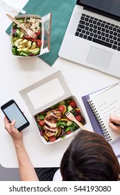 Overhead Of Busy Working Person At Workstation With Takeaway Food And Laptop, Hands On Phone