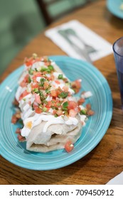 Overhead Close Up Of A Large Mexican Breakfast Burrito Smothered In Fresh Tomato Pico De Gallo Salsa And Covered With Sour Cream With Blurry Restaurant Table Background