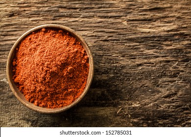 Overhead Close Up View Of A Bowl Of Ground Red Cayenne Pepper On A Weathered Heavily Textured Wooden Background With Copyspace