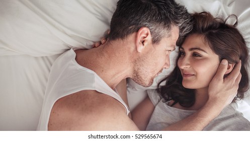 Overhead close up of young couple lying in bed together. Romantic couple in love looking at each other.