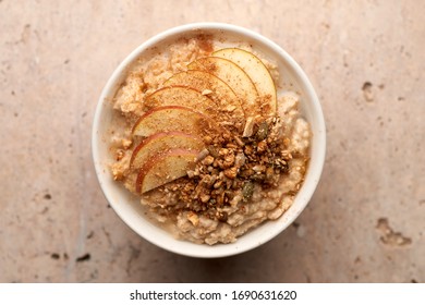 Overhead Closeup Of A Bowl Of Oatmeal Or Porridge Topped With Apple Slices, Cinnamon, And Granola