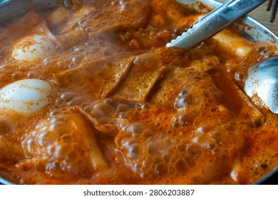 An overhead close-up shot capturing the intense boiling texture, rich bubbles, and steam of a Korean Tteokbokki pot filled with sliced fish cakes and boiled eggs