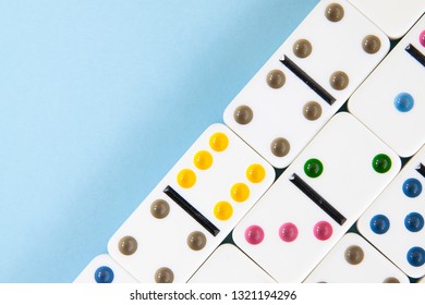 Overhead Closeup Of White Dominoes With Brightly Colored Dots On A Blue Background With Copy Space