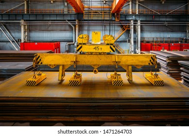 Overhead crane with electromagnetic beam grippers lifting steel sheets.