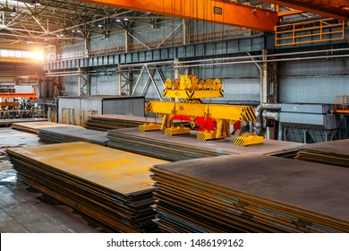 Overhead crane with electromagnetic beam grippers lifting steel sheets.