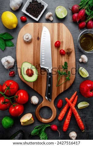 Overhead dark tabletop image of real colorful healthy nutritious raw vegetable and fruit plant-based vegetarian and vegan diet foods placed on a wood cutting board with a clean kitchen knife.