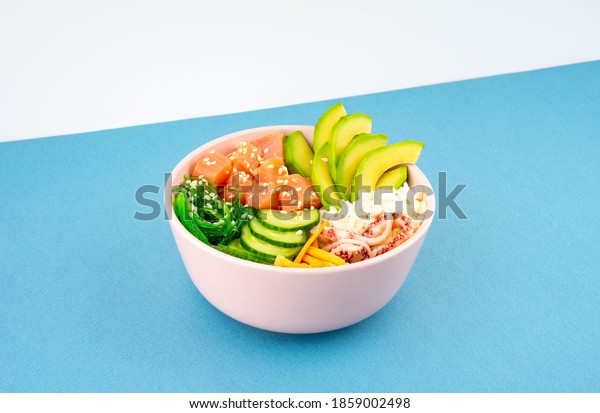 An overhead diagonal, isometric projection photo
of poke bowl, traditional Hawaiian and Japanise raw fish salad,
from seaweed, rice, salmon, cucumber, soy sause and avocado. with
chopsticks and sesame