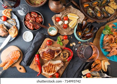 Overhead Of Dinner Table. Barbecue Meat And Seafood With Vegetable. Pork Grilled Steaks, Grilled Salmon Trout, Mussels, Shrimps, Dried Tomato, Cherry Tomato,  Glass Of  Wine. Picnic Bbq Party Concept.