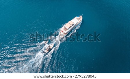 An overhead drone shot captures a large white yacht and two smaller speedboats creating wakes as they travel across the vast, clear blue sea