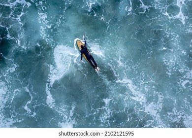 An overhead drone shot of a surfer in the wavy sea, Newport Beach, California, USA - Powered by Shutterstock