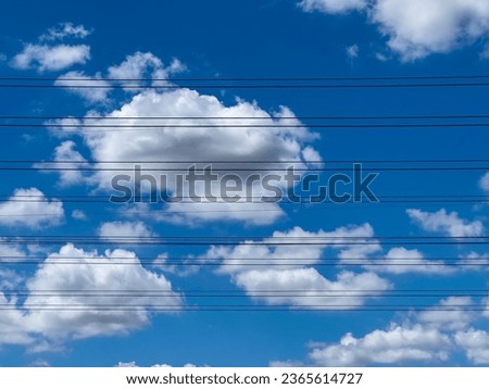 Overhead electrical and communication cables across partly cloudy blue sky above a suburban parking lot (off camera), for motifs of technology and connectivity, infrastructure, and the environment