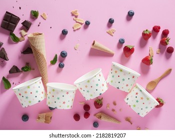 Overhead Empty Ice Cream Cups And Cones. Concept Of Variety Of Flavors. Chocolate Chunks, Mint Leaves, Strawberries, Raspberries And Blueberries On A Pink Background.