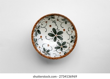 Overhead flat lay of decorative ceramic bowl with simple floral pattern and natural tones, isolated on white background, photographed using soft diffused lighting and clean composition.